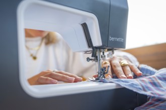 Sewing process with a sewing machine in a close-up, emphasised by the guiding hands with jewellery
