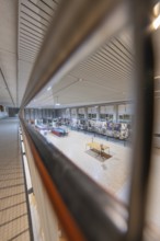 Through a railing you look at an exhibited collection of artworks under a modern structured