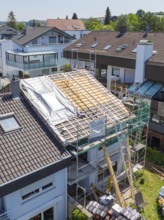 A roof is being renovated or newly built, scaffolding visible, sunny neighbourhood, roof