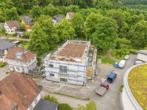 Building under construction with scaffolding, surrounded by trees and construction site vehicles,