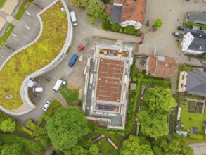 Bird's eye view of building with roof, surrounded by trees and construction site activities,