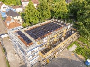 Building under construction with solar cells on the roof, surrounded by houses and trees, Hirsau,