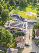 Building under construction with solar modules and green roof, embedded in a green environment,