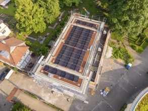 Roof of a construction site with solar cells, surrounded by trees and other buildings, modern
