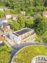 Aerial view of a construction site in a residential area surrounded by trees and green roofs on a