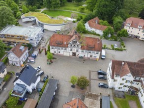 Historic half-timbered houses with red tiled roofs surrounded by cobblestones and green spaces,