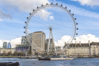 The london eye majestically stands tall on the banks of the river thames, with a boat sailing by