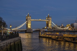 Tower bridge stands majestically illuminated against the twilight sky, its lights reflecting on the