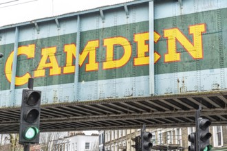 Camden town sign painted on a railway bridge in london, featuring a green light and urban buildings