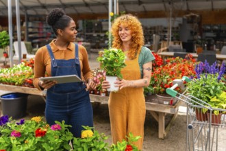 Two young women working in a garden center, discussing plants and using a digital tablet for