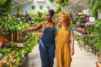 Two young women walking through a garden center, discussing plants and sharing knowledge while