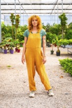 Confident young farmer standing amidst lush greenery in a greenhouse, overseeing her thriving