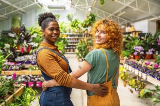Two happy florists are hugging each other, smiling, while working in their plant nursery greenhouse