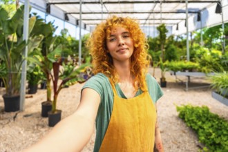 Confident red haired female gardener taking a selfie in a greenhouse, showcasing her passion for