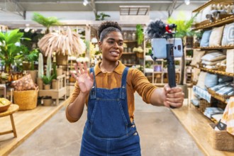 Young saleswoman waving and streaming live video using a smartphone and microphone inside a