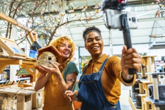 Two cheerful female shop assistants filming a vibrant video for social media while showcasing a