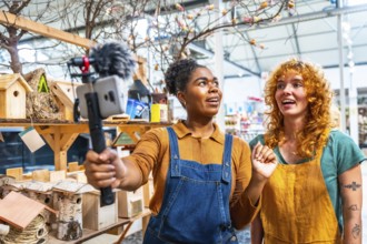 Two young women working in a garden center filming a video for social media using a smartphone with