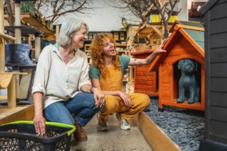 Smiling saleswoman showing a wooden dog house with a dog statue inside to a customer holding a