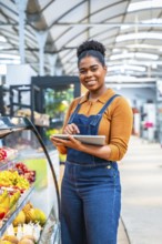Young supermarket employee managing fresh fruit section inventory using a digital tablet, ensuring