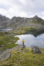 Mountaineer on a rock in front of mountain lakes Wangenitzsee and Kreuzsee, cloudy mountain peaks