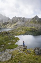 Mountaineer on a rock in front of mountain lakes Wangenitzsee and Kreuzsee, cloudy mountain peaks