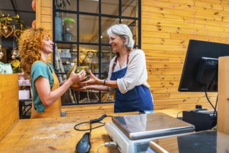 Two women joyfully exchanging a pumpkin in a vibrant flower shop, with a scale and computer