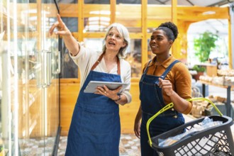 Two supermarket workers using digital tablet and basket, managing inventory and ensuring efficient