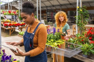 Two young women working in a garden center, taking care of plants and using a digital tablet for