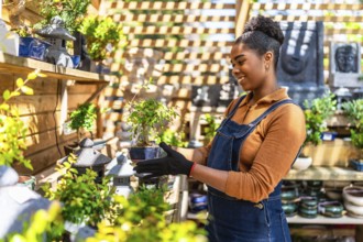 Smiling young woman working in a vibrant plant shop, holding a small bonsai tree and showcasing her