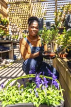 Young woman working in a vibrant greenhouse, holding a small bonsai tree, surrounded by flourishing