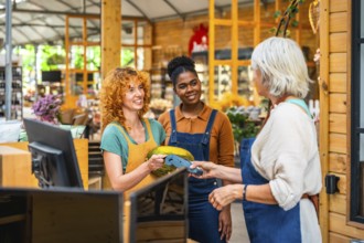 Customer paying with contactless payment in a grocery store, assisted by two smiling shop
