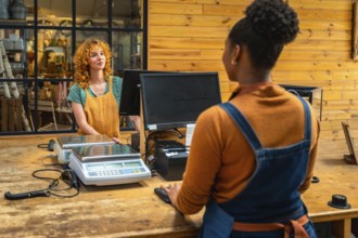 Female shop assistant serving customer at checkout counter in flower shop, using computer and