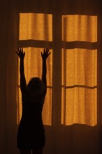 Back view of a woman with raised hands standing in front of a window with a red curtain