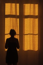 Back view of a woman standing in front of a window with a red curtain