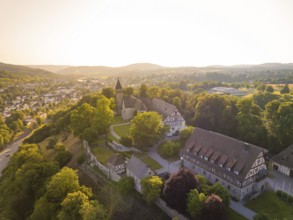 An idyllic village with a church, half-timbered houses and lush forest in warm sunlight, event and