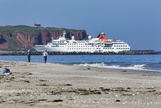 Tourists and photographers on the beach of the Heligoland dune, cruise ship in front of cliffs,