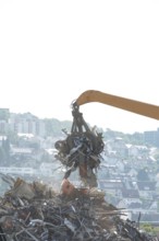 Hydraulic crane lifts scrap metal at the scrapyard in the background a city