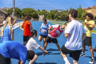 Teenage athletes stretching their legs and arms on a vibrant blue track, engaging in warm up