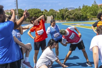Teenagers wearing bib numbers stretching together on a blue running track before a track and field