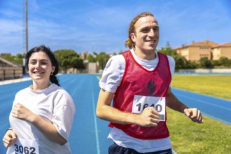 Two happy athletes running a race on a blue track at an athletics stadium under a clear blue sky