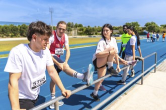 Runners stretching their legs on a railing, preparing for competition on an athletics track under a