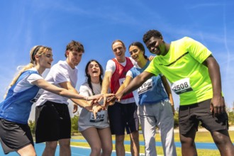 Diverse group of young athletes putting their hands together before a track and field competition,