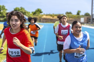 Teenage track and field athletes running on a blue track during a competition, wearing bibs with