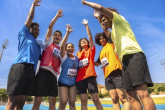 Group of young runners celebrating their victory with arms raised high after crossing the finish