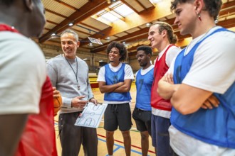 Basketball coach holding clipboard and explaining game strategy to his team players in a gymnasium