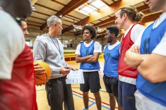 Basketball coach holding ball and clipboard explaining game strategy to diverse team players in