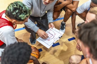 Basketball coach discussing game strategy with his team on a clipboard during a timeout, fostering