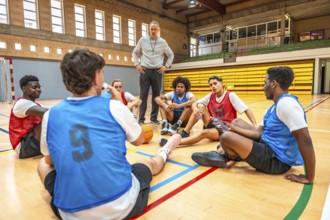 Basketball coach standing and talking to his team players sitting in a circle on the court during a
