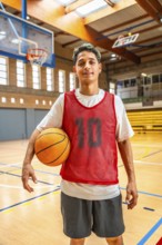 Energetic young basketball player holding a ball on an indoor court, wearing a red jersey, ready