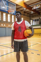 Young male basketball player holding a ball while standing confidently on a polished wooden court